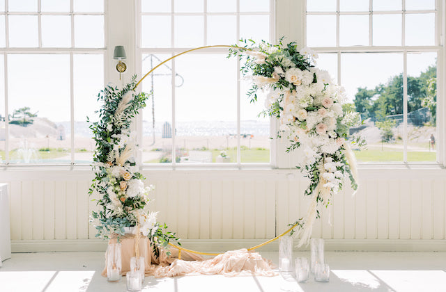 Näyttävä kultainen vihkikaari somistettuna kukilla ja kankailla.