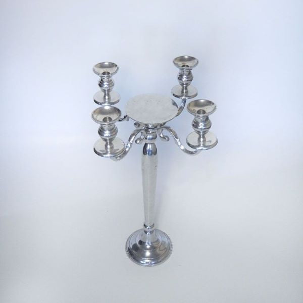 Näyttävä hopeinen nelihaarainen kynttelikkö kruunaa juhlien somistuksen. Keskelle kynttelikköä tolppakynttilälle paikka, jonka halkaisija on 15 cm. Kyttelikköön sopii max 2,2 cm halkasijaltaan olevat kruunukynttilät.